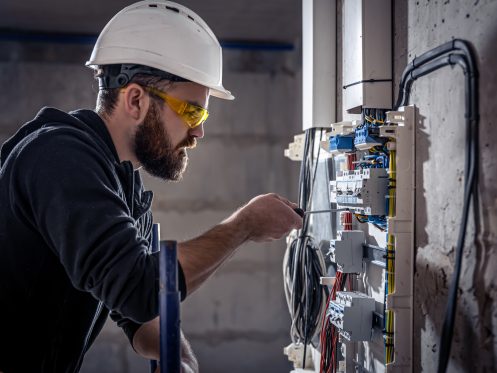 An electrician works in a switchboard with an electrical connecting cable, connects the equipment with tools.